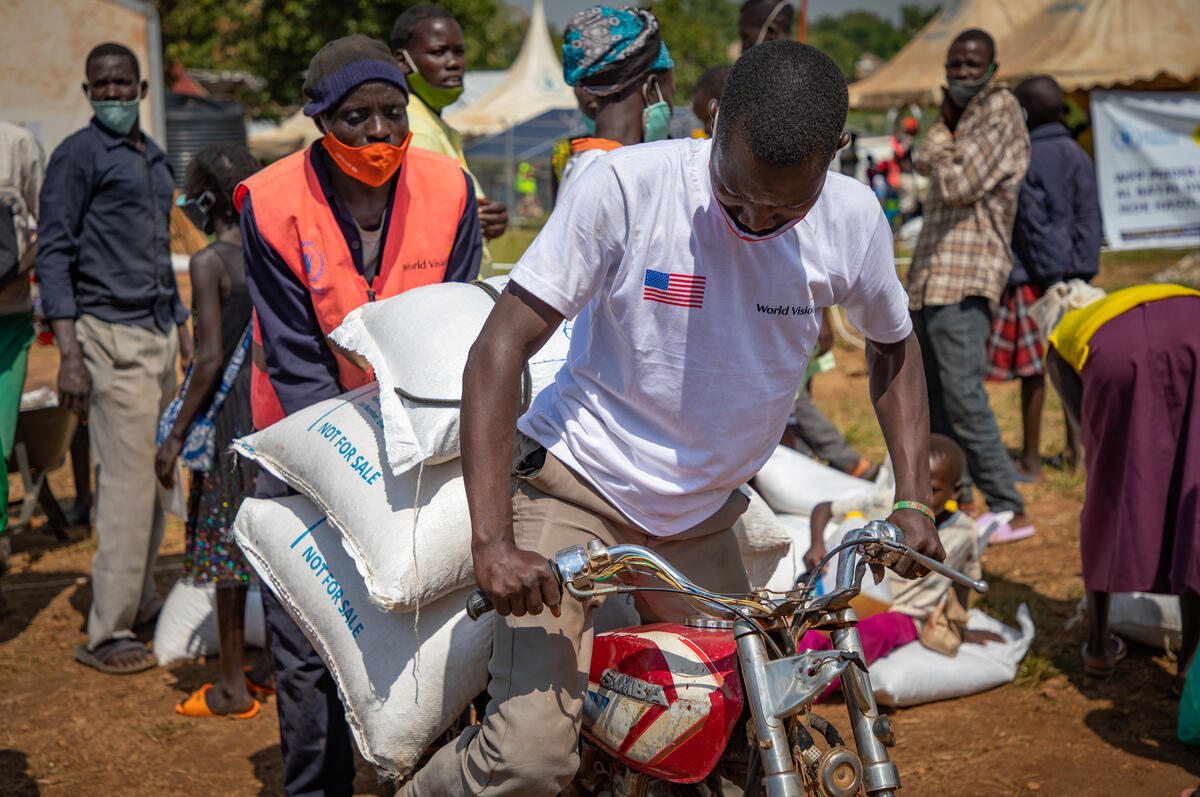 Angelo es ayudado por un porteador en el punto de distribuci&oacute;n para cargar su comida en una motocicleta.